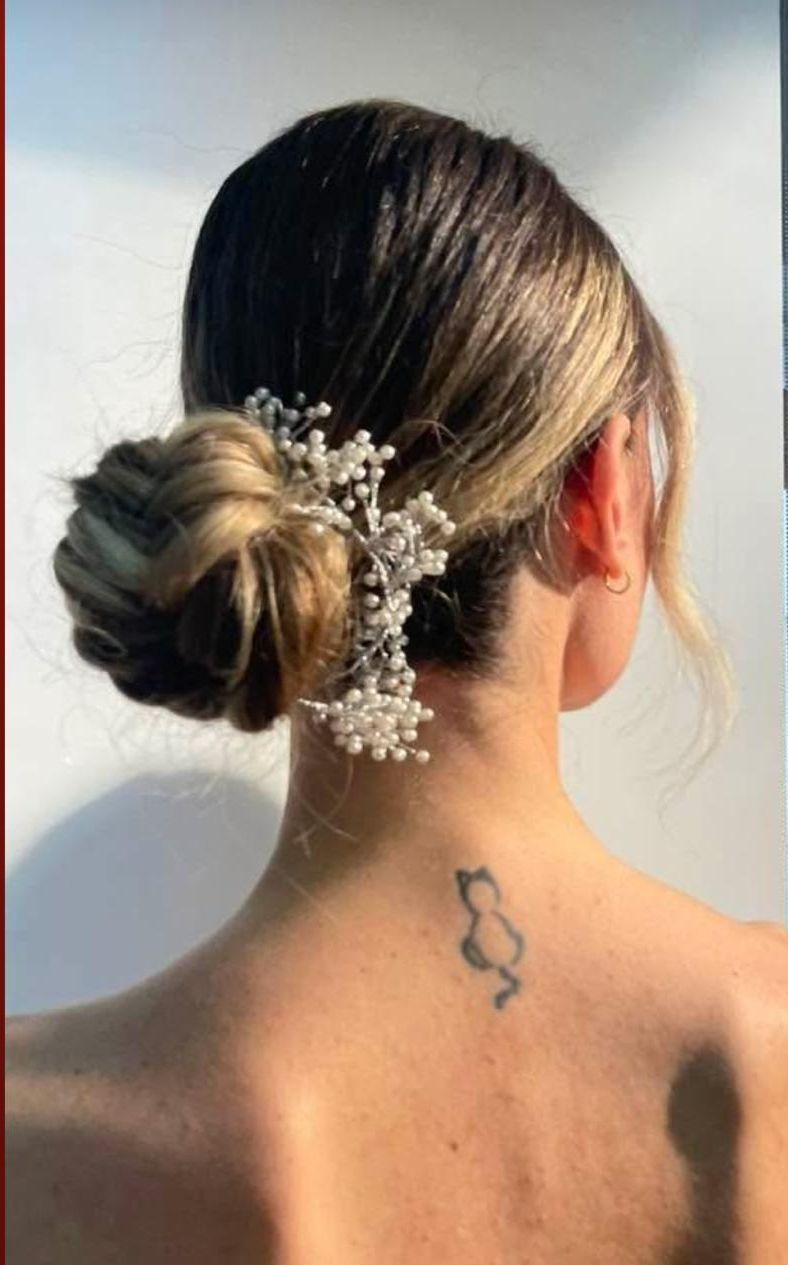 Acconciatura raccolta da donna con accessorio per capelli di perle e un piccolo tatuaggio di un gatto sulla nuca.