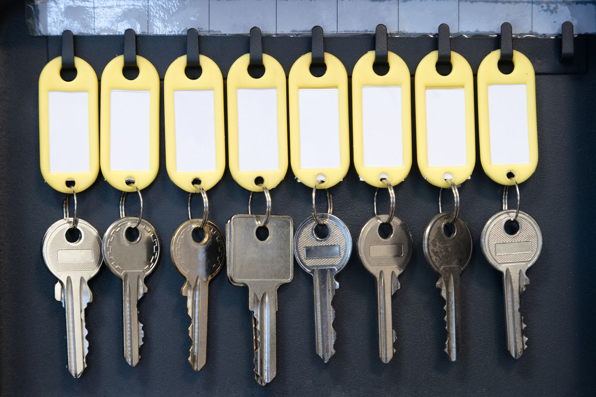 Nine keys hanging from a rack, each with a yellow tag for labeling.