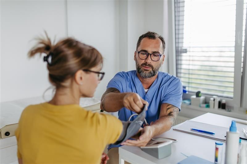 Male doctor measuring a female patient's blood pressure at an urgent care clinic.