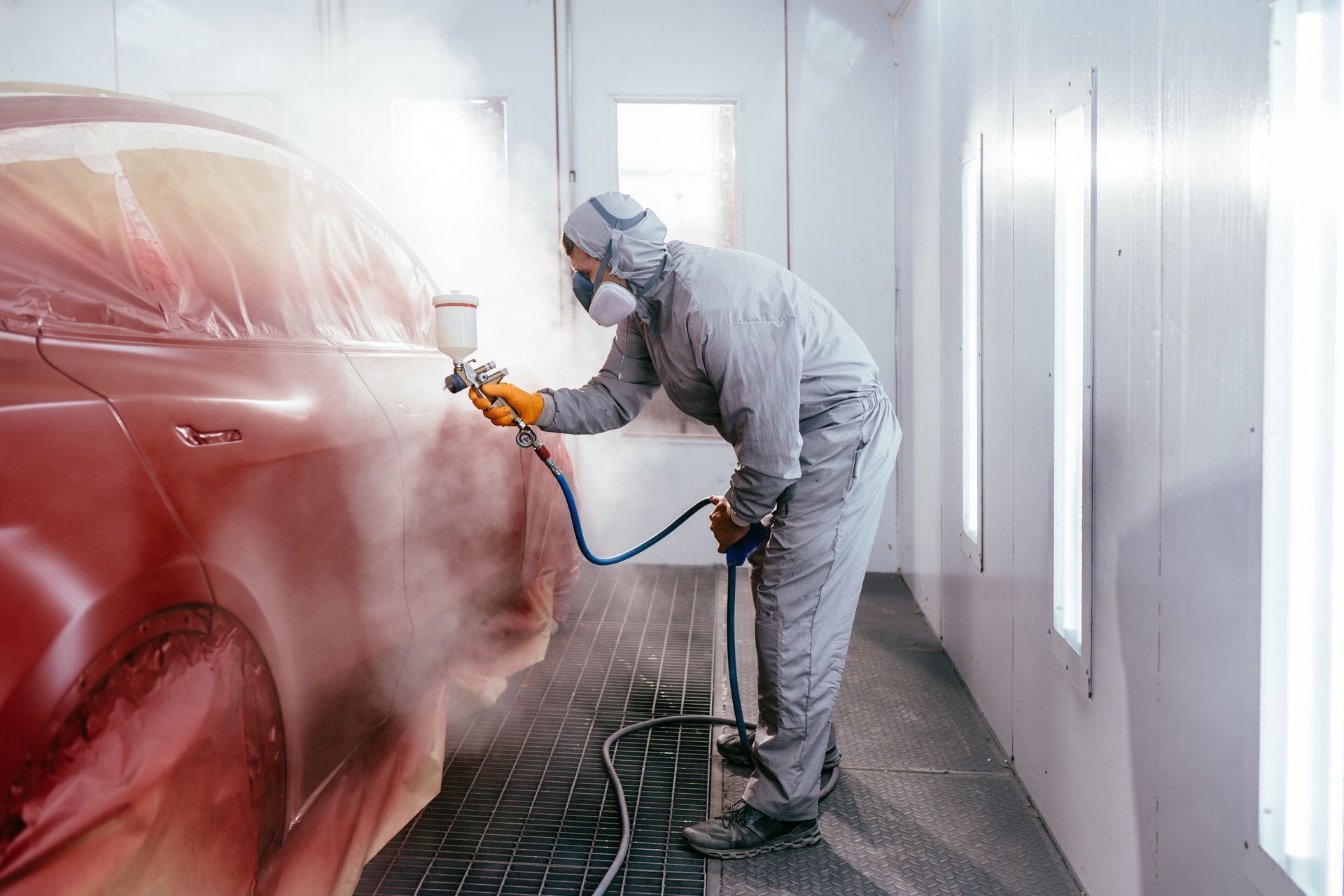 A man is painting a red car in a paint booth.