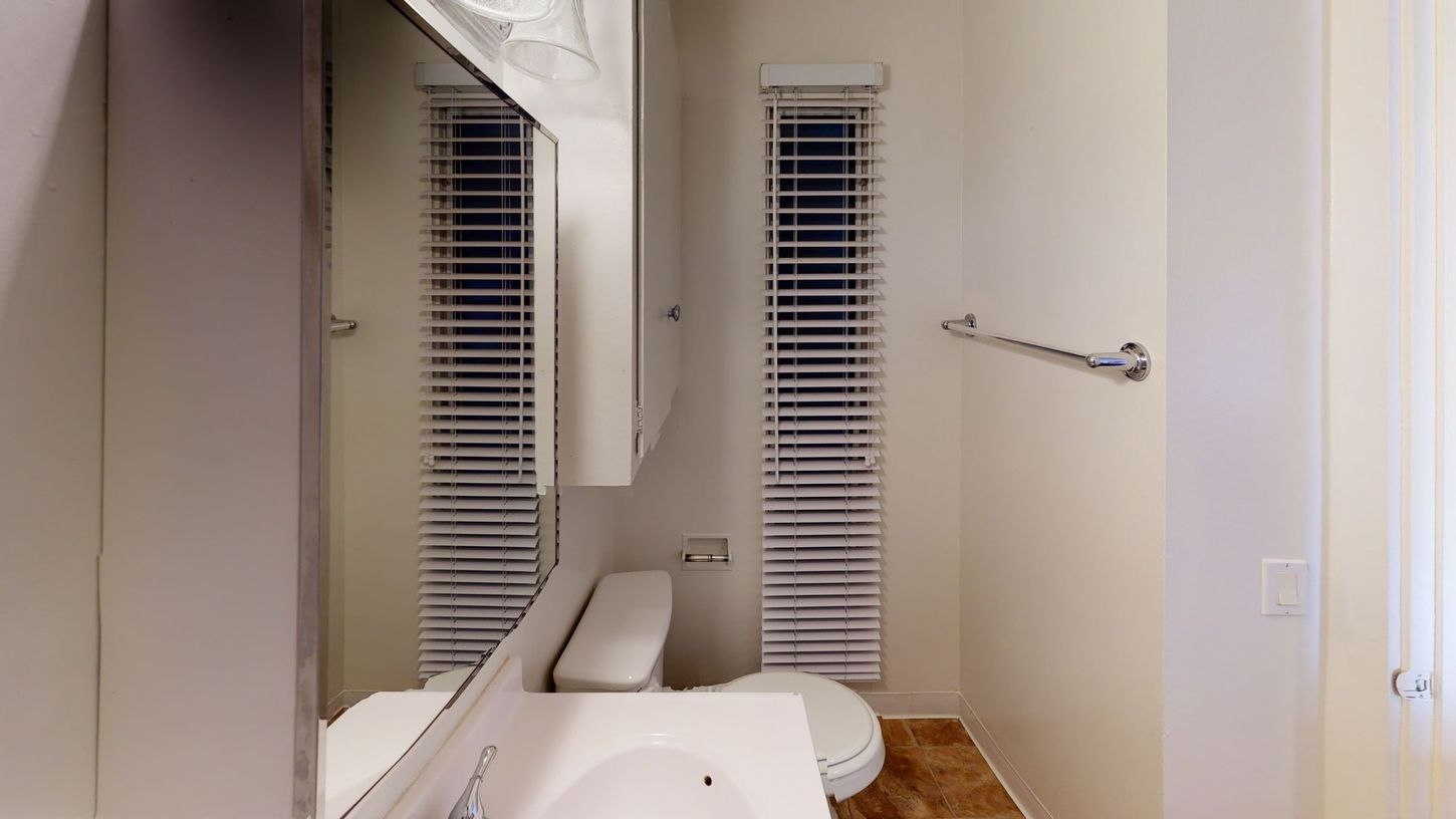 Bathroom with toilet, sink, mirror, blinds, and towel rack.