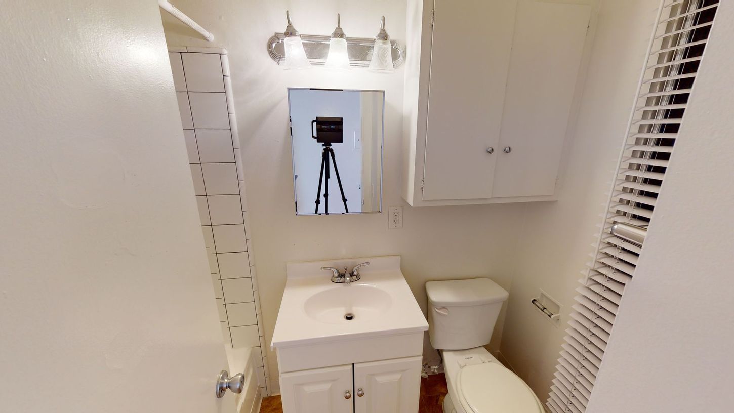 Small bathroom with sink, toilet, mirror, and cabinet. White walls and fixtures.