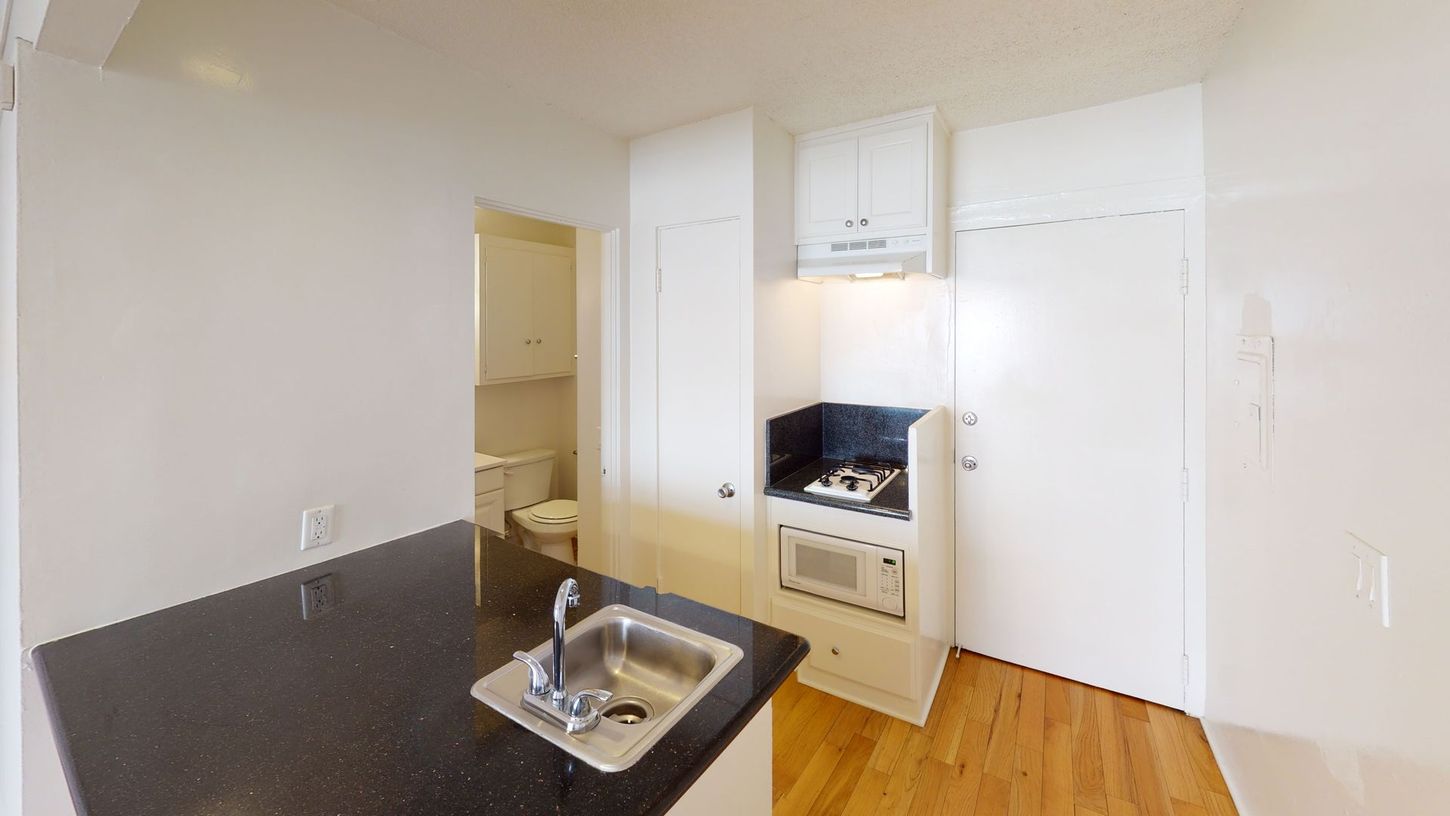 Small kitchen with black countertop, white cabinets, sink, and stove. Doorway to a bathroom.