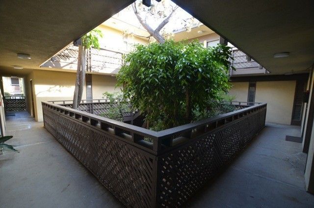 Indoor courtyard with a wooden enclosure for plants, surrounded by a walkway with apartment doors.