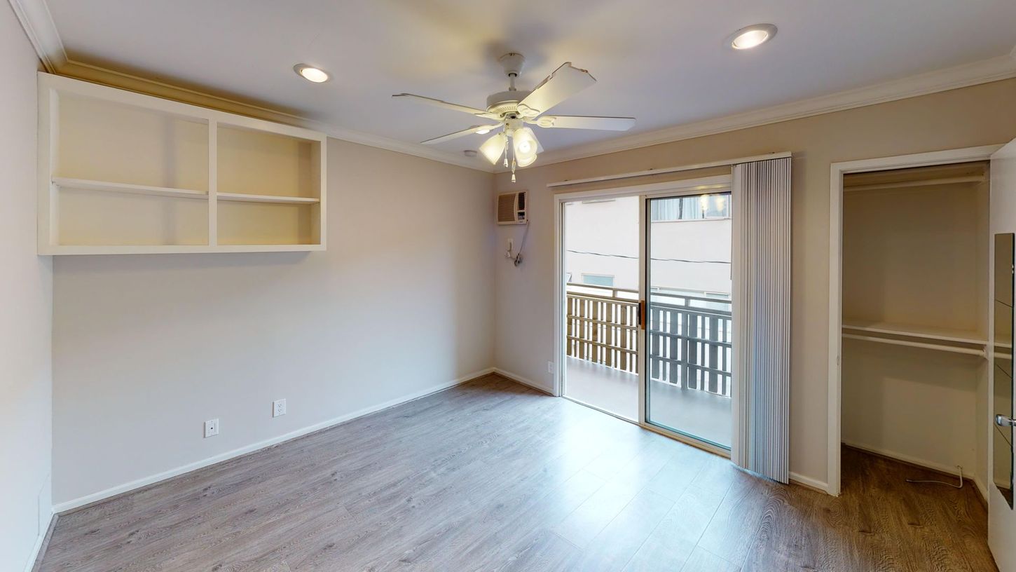 Empty bedroom with white walls, sliding glass door to balcony, built-in shelves.