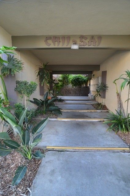 Covered walkway entrance with concrete steps and greenery.