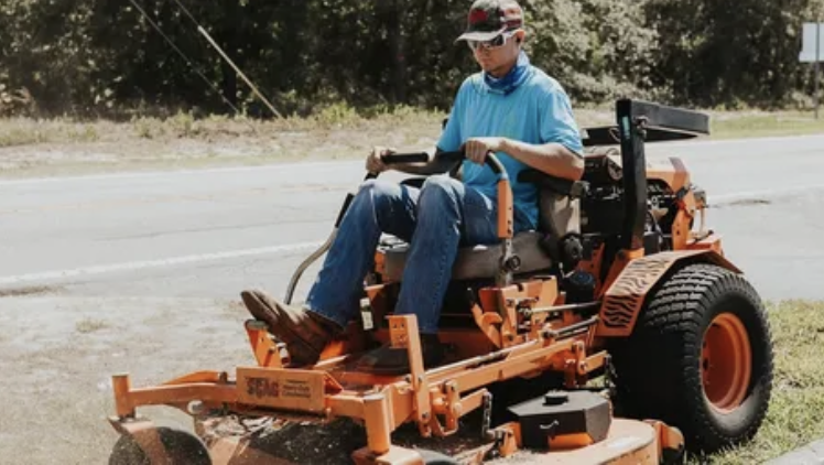 Carson Gotts riding an orange lawn mower while mowing grass.