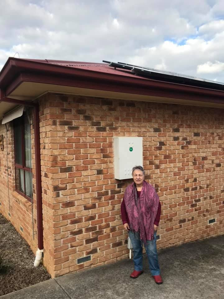 Woman is Standing in Front of A Brick House With Solar Panels on The Roof — EV Chargers in Lake Gardens VIC