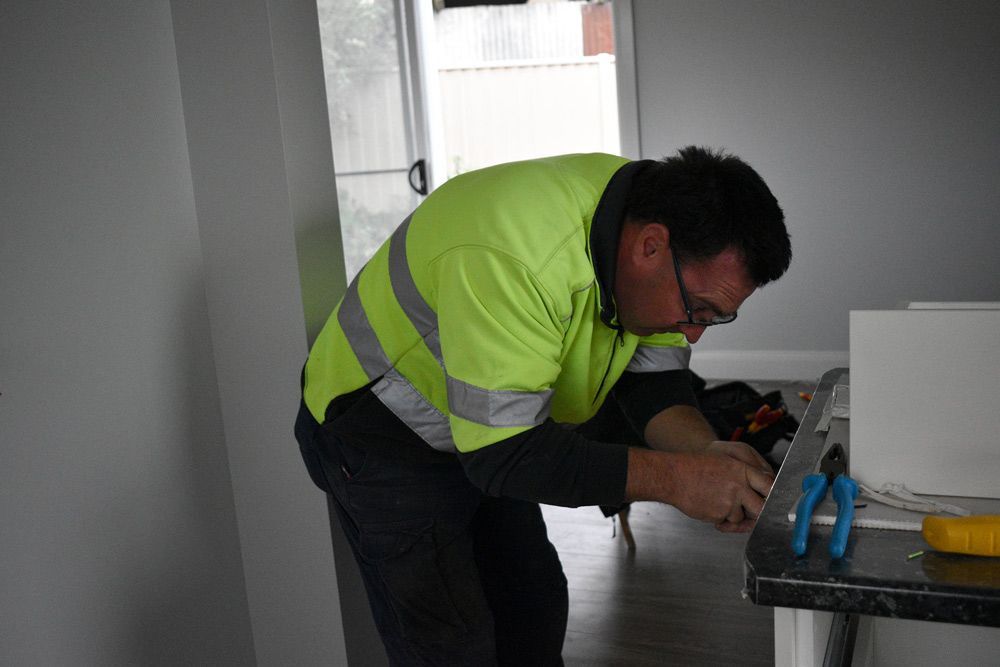 Electrician in a yellow vest is working on a wire — Electrical Services in Lake Gardens VIC