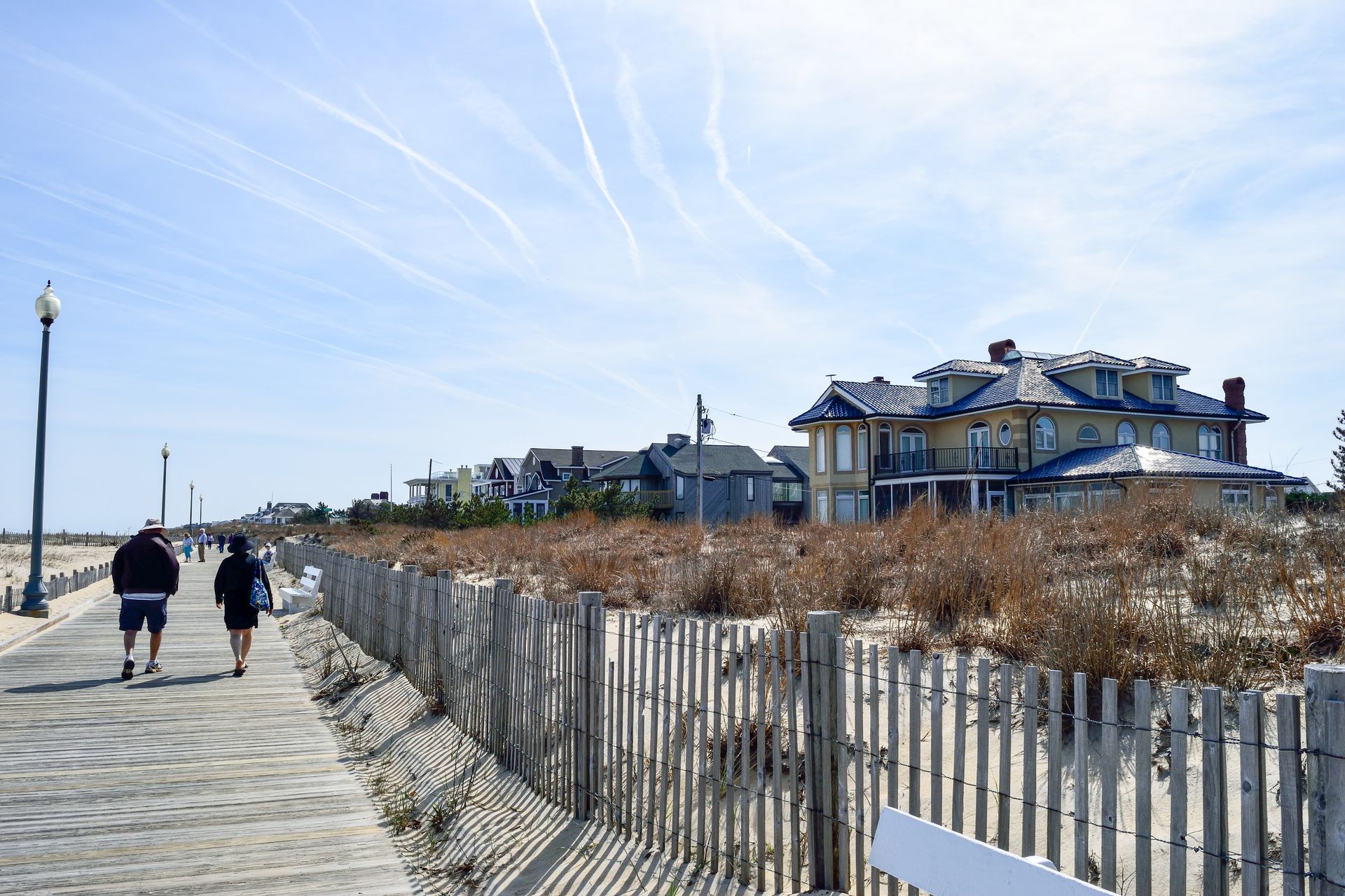 A couple of people are walking down a boardwalk next to a fence.