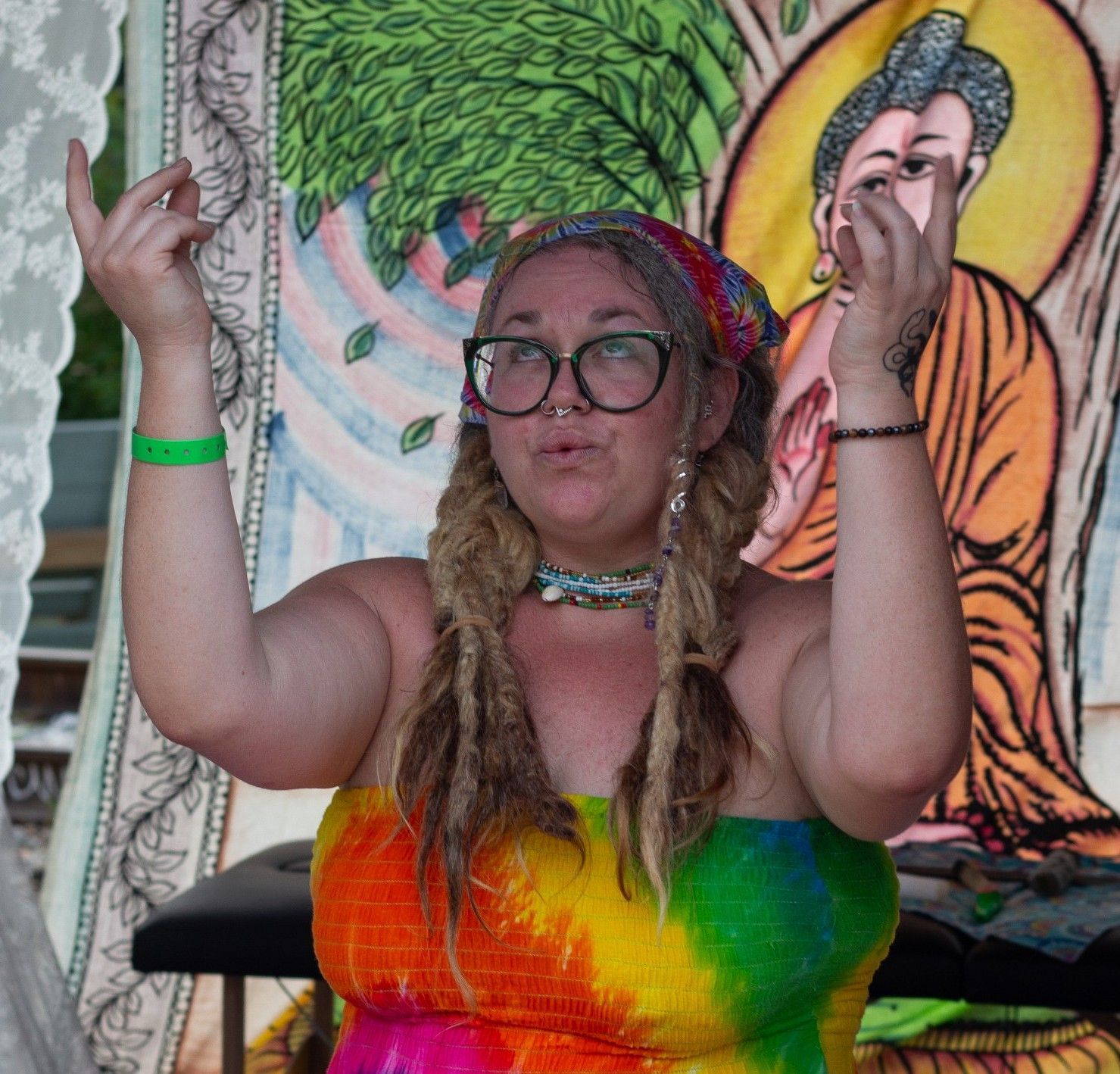 a woman wearing glasses and a rainbow colored dress, with her hands lifted up