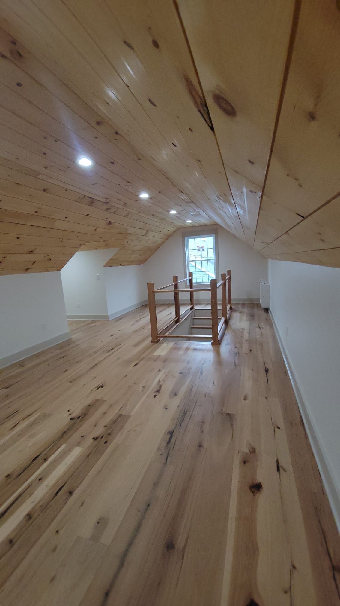 Loft with wood floors and ceiling, white walls, and a small window.