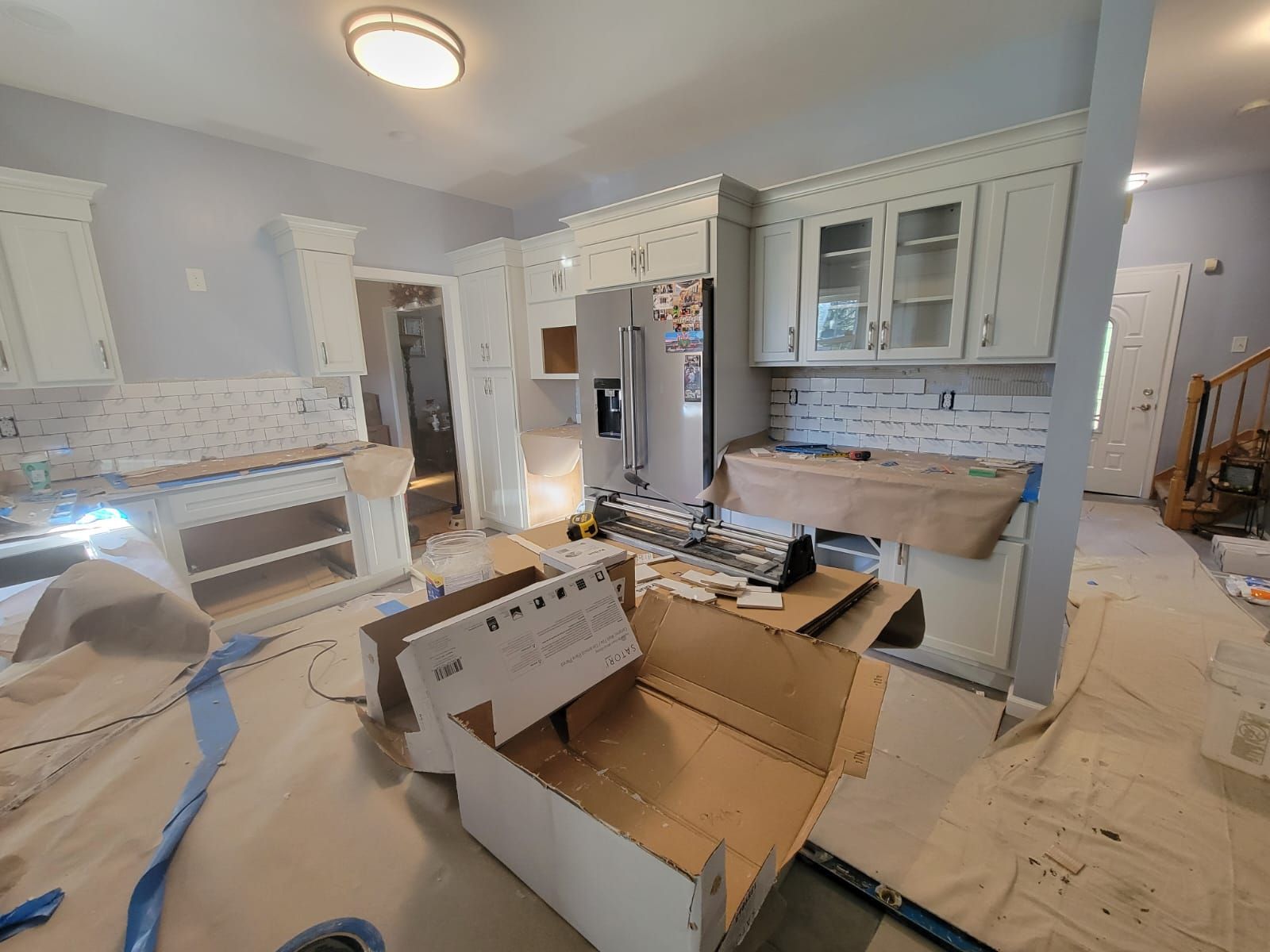 Kitchen renovation in progress: cabinets, refrigerator, and backsplash. Boxes and protective coverings on the floor.