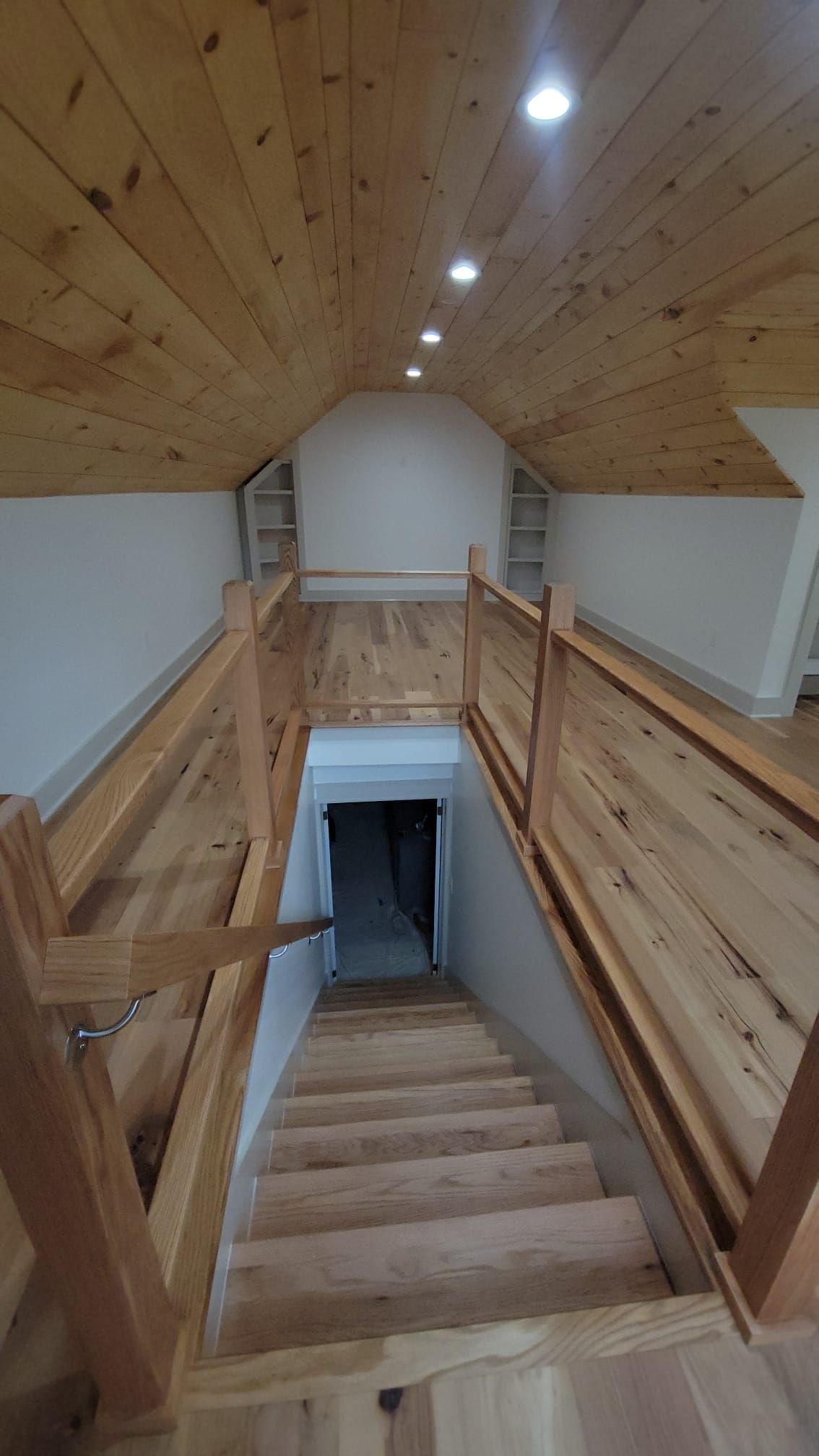 Wooden staircase leading to a dark doorway; light-colored wooden ceiling and railing.