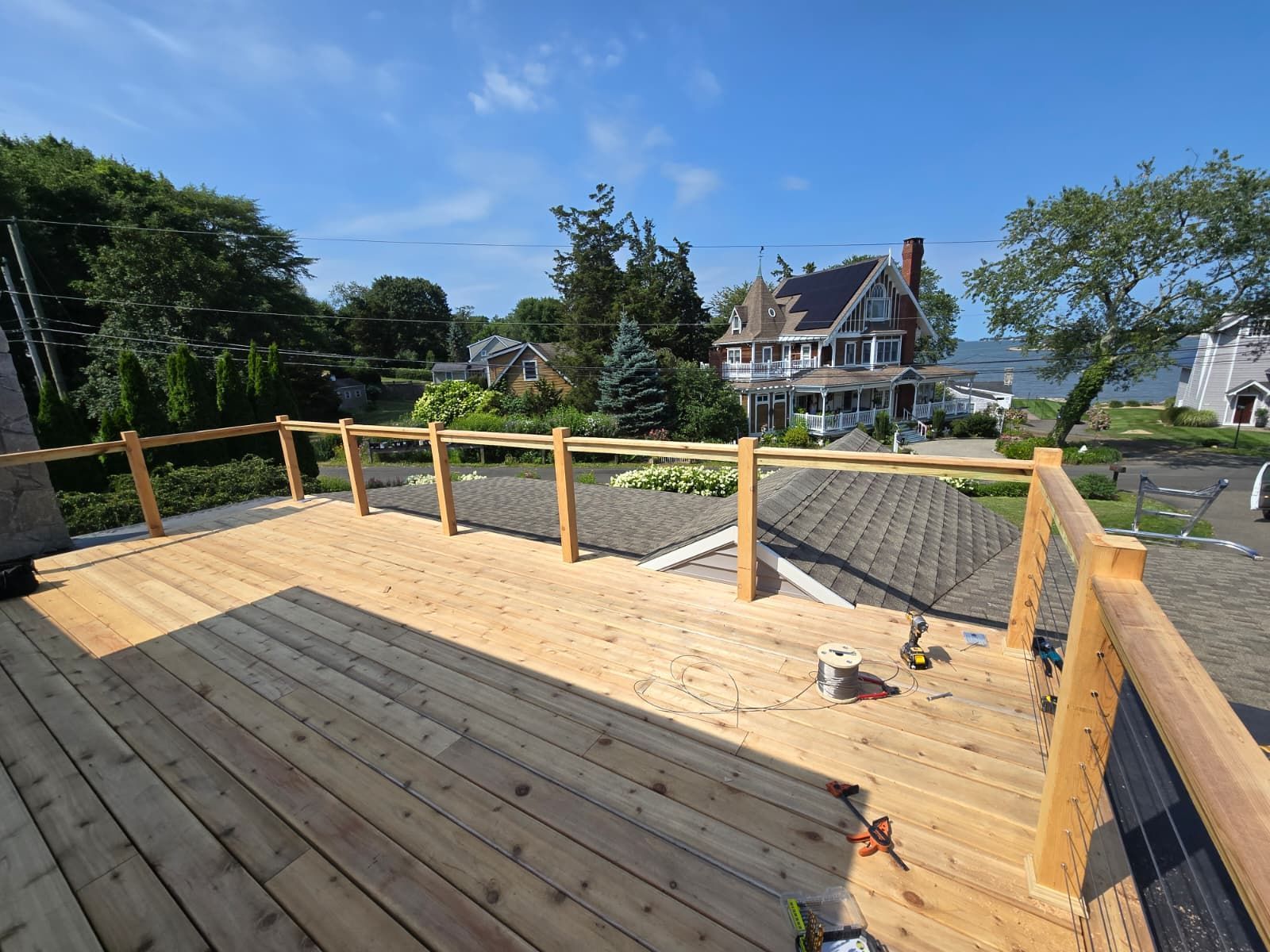 Wooden deck with railing overlooking houses and water on a sunny day.