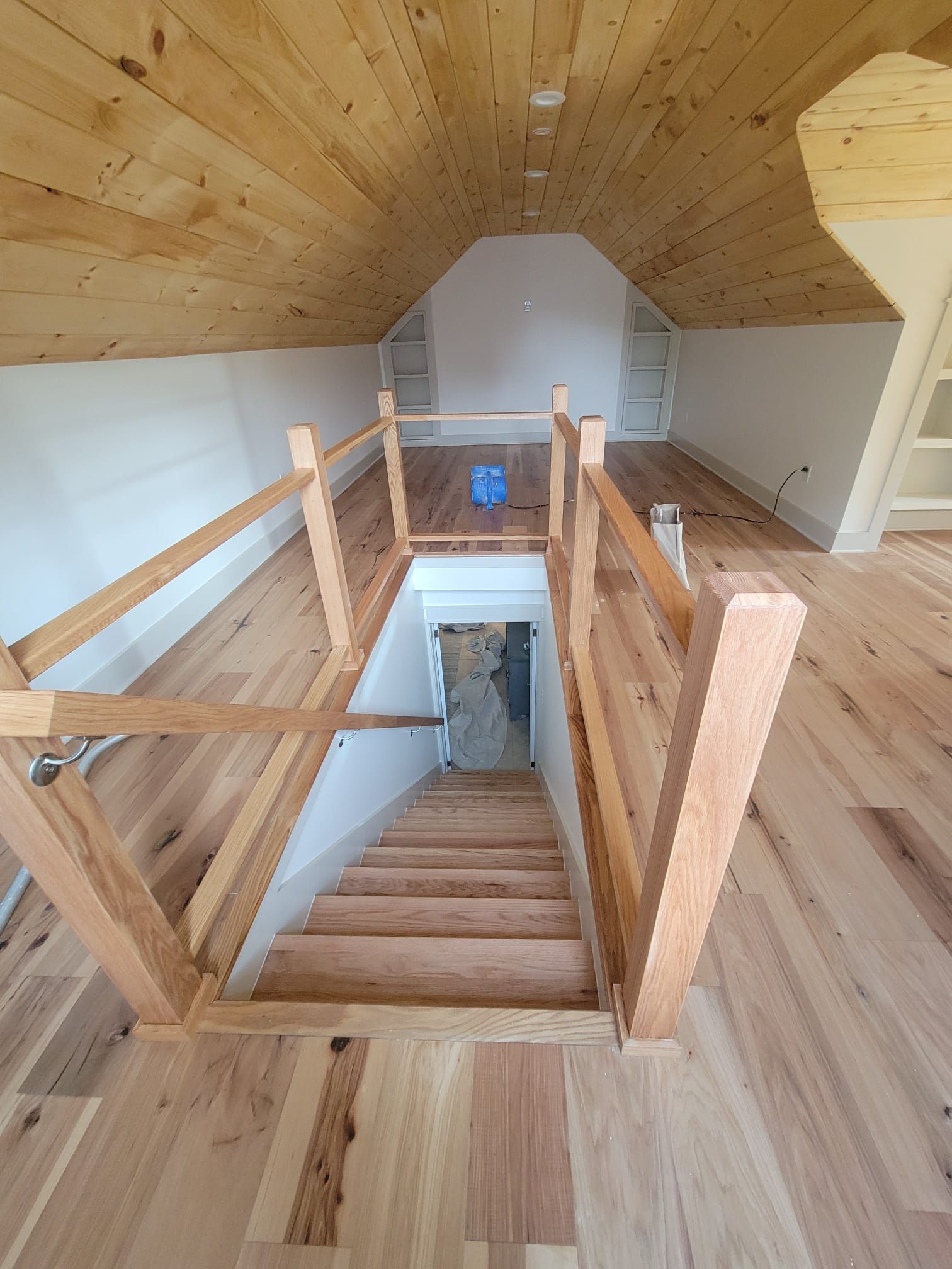 Interior with wooden stairs leading up to a loft with wooden floor and ceiling. White walls, wooden railing.