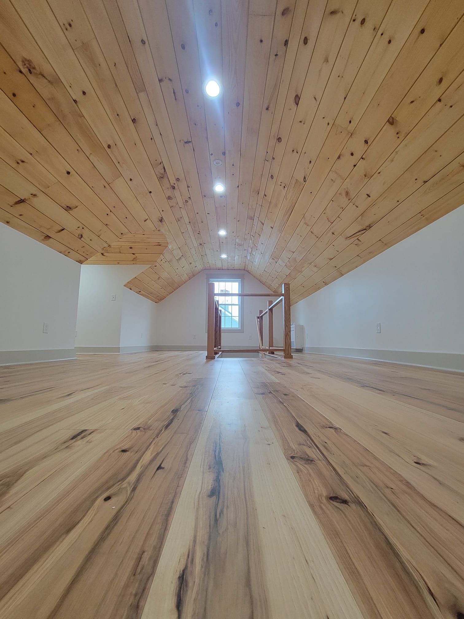Loft interior with wooden floor and ceiling, white walls, and small window at the end.