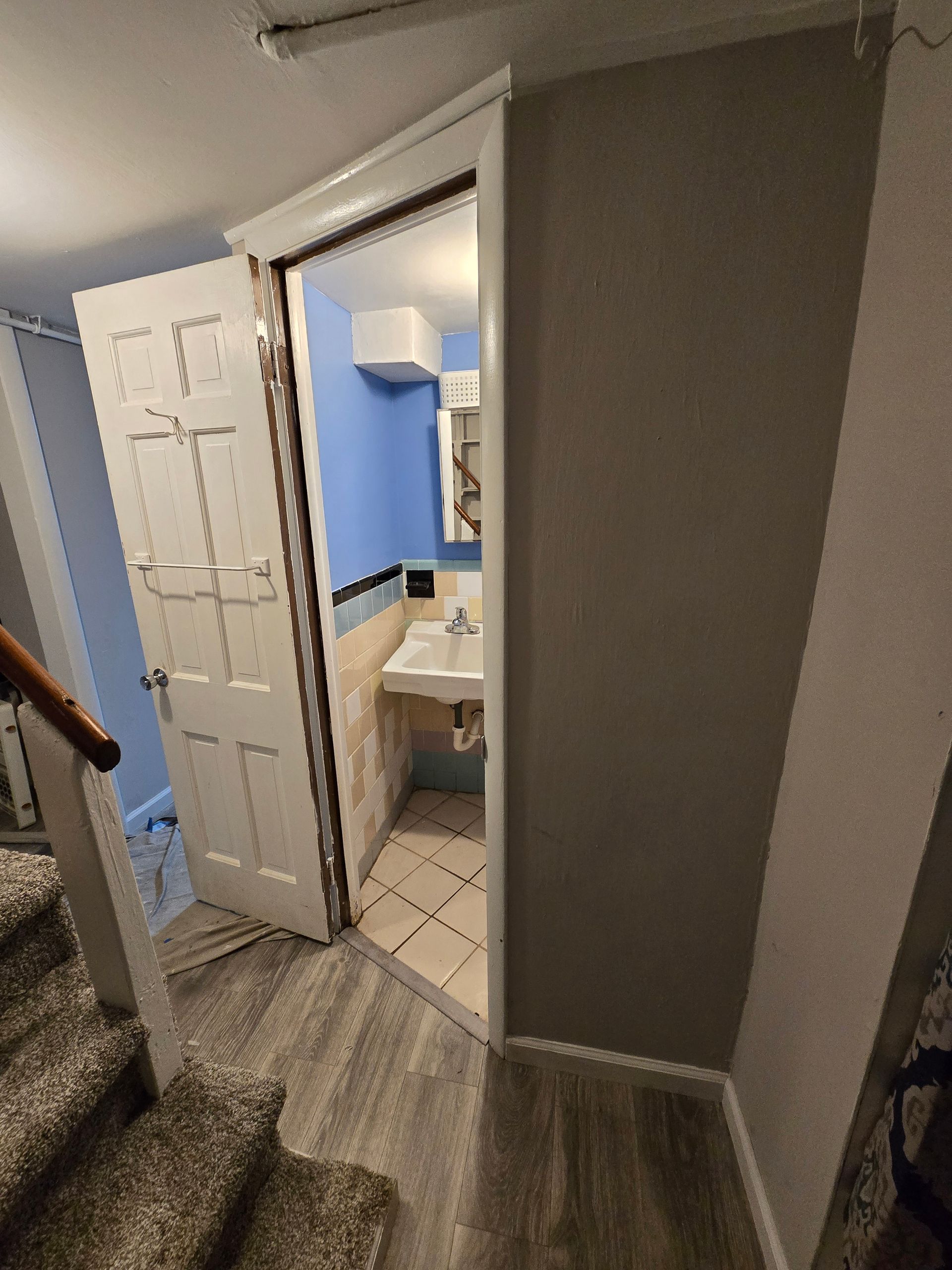 Bathroom doorway with open white door, blue wall inside. Stairs on the left.