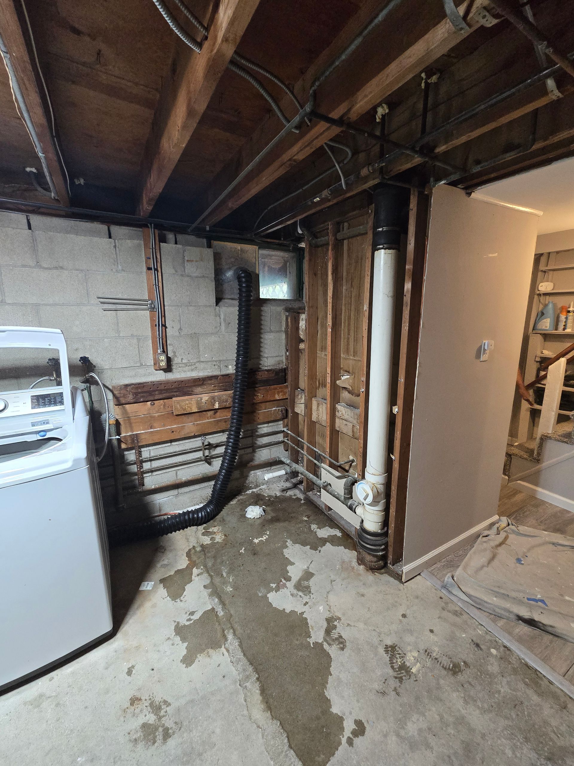 Basement with unfinished walls, exposed pipes, and a washing machine, concrete floor is wet.