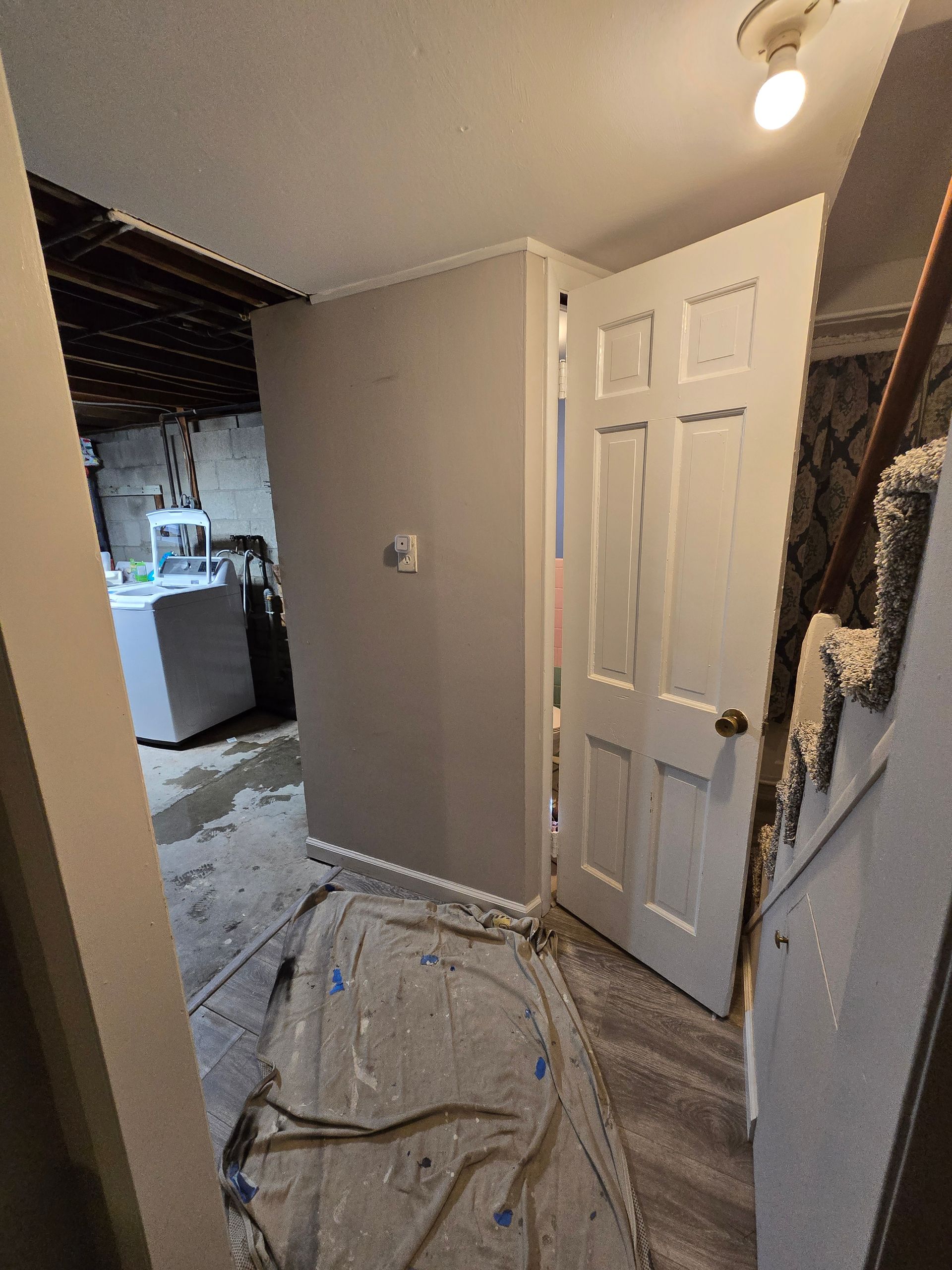 Basement hallway with a gray wall, open white door, and laundry area in the background.