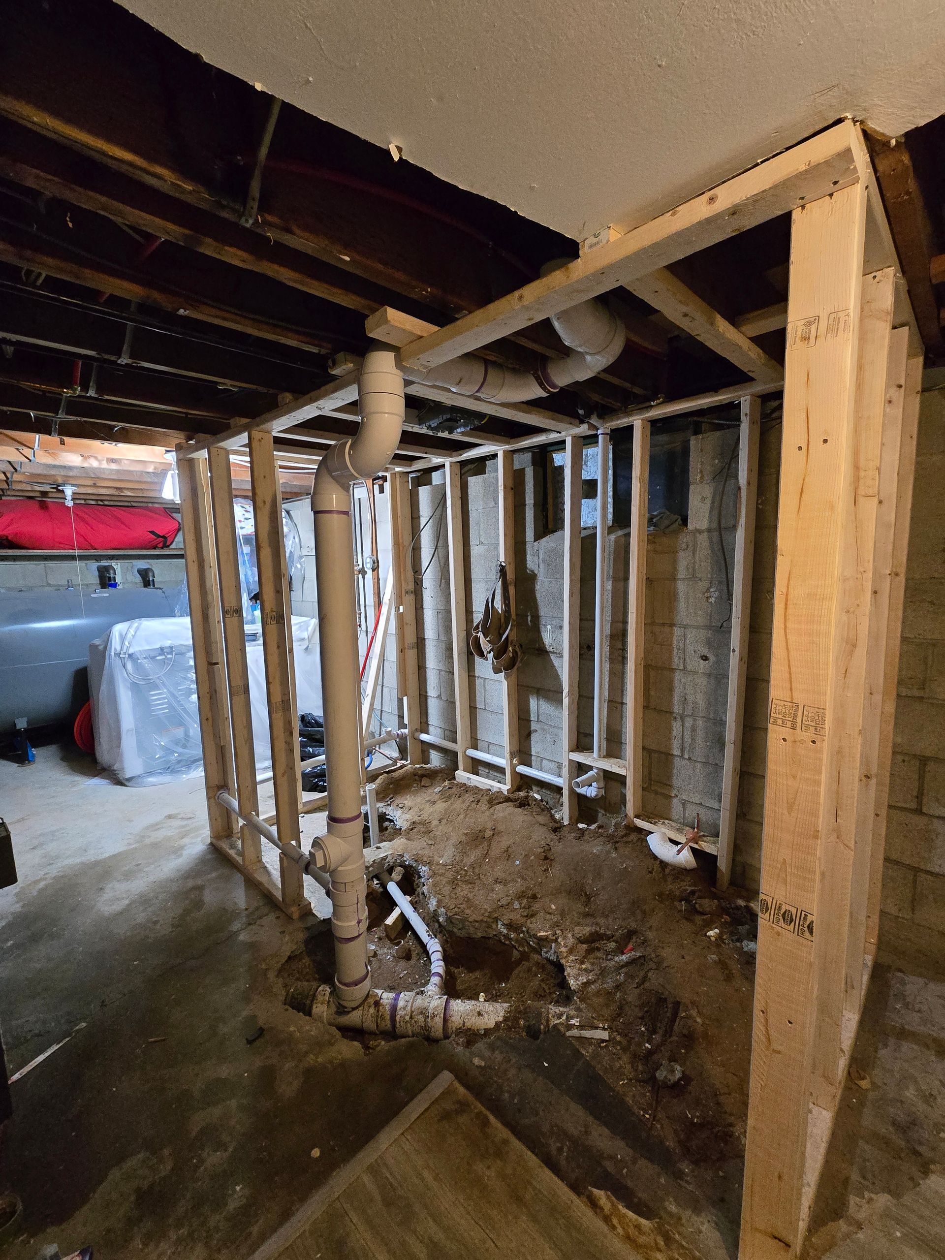 Framed wooden walls under a basement ceiling, with exposed plumbing pipes and dirt floor.