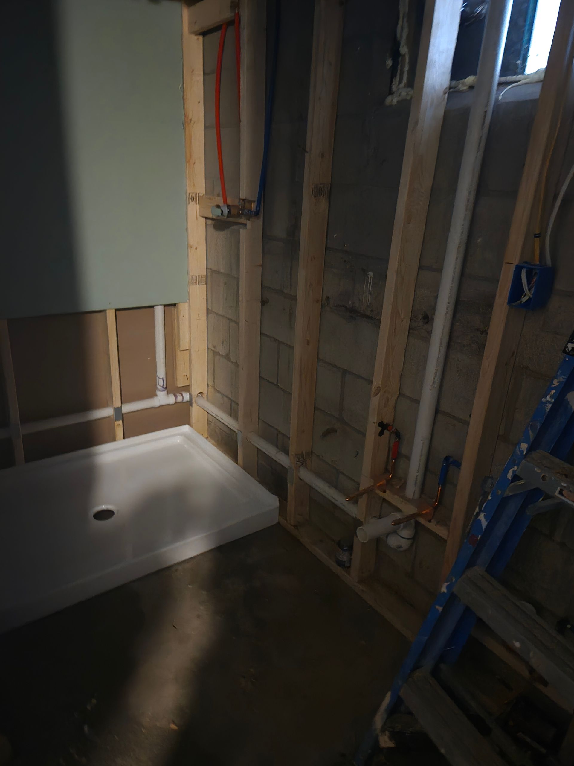 A partially constructed basement bathroom, with a shower base, framing, and plumbing visible.