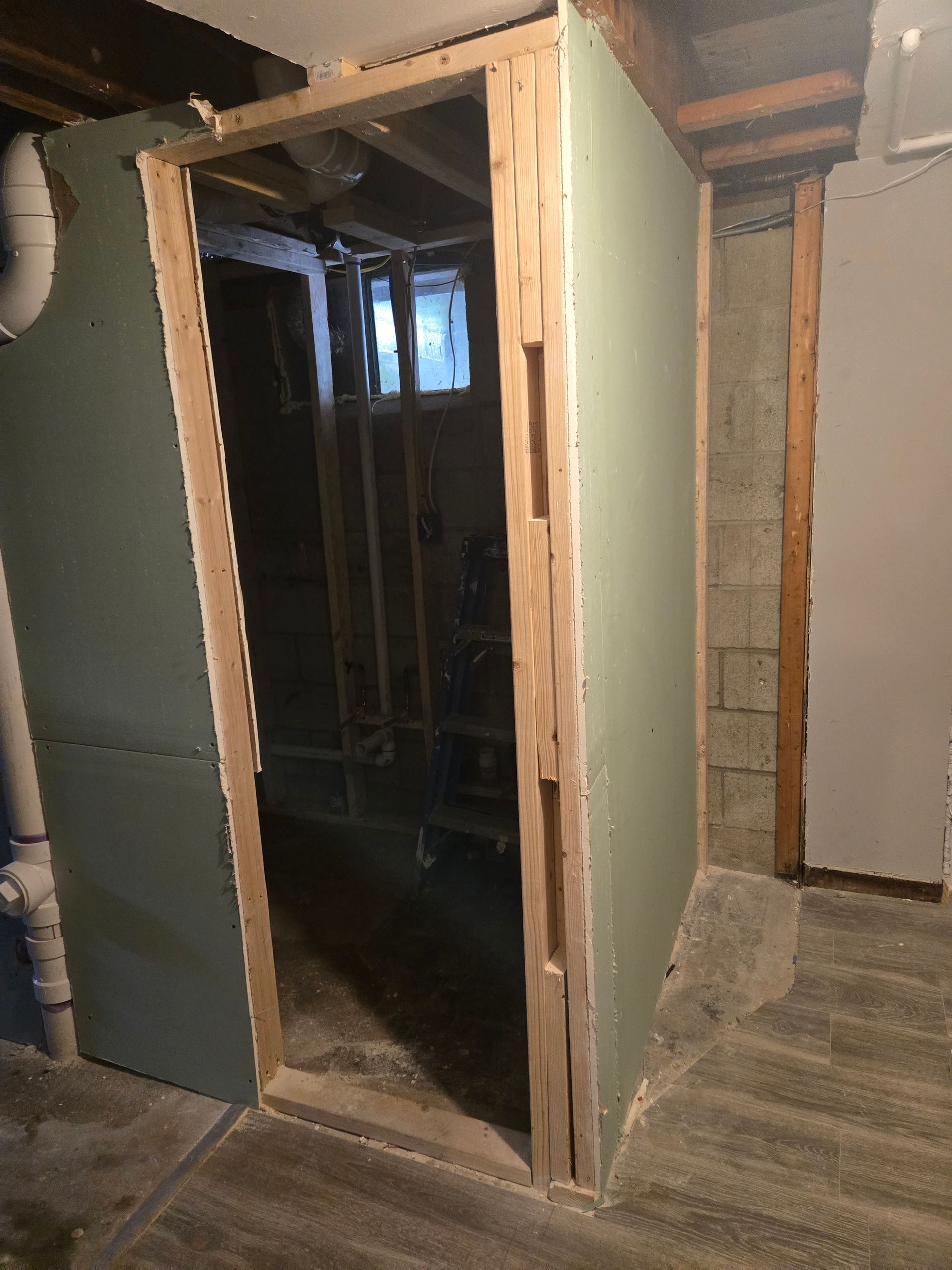 Basement doorway under construction with green drywall and exposed wood framing.