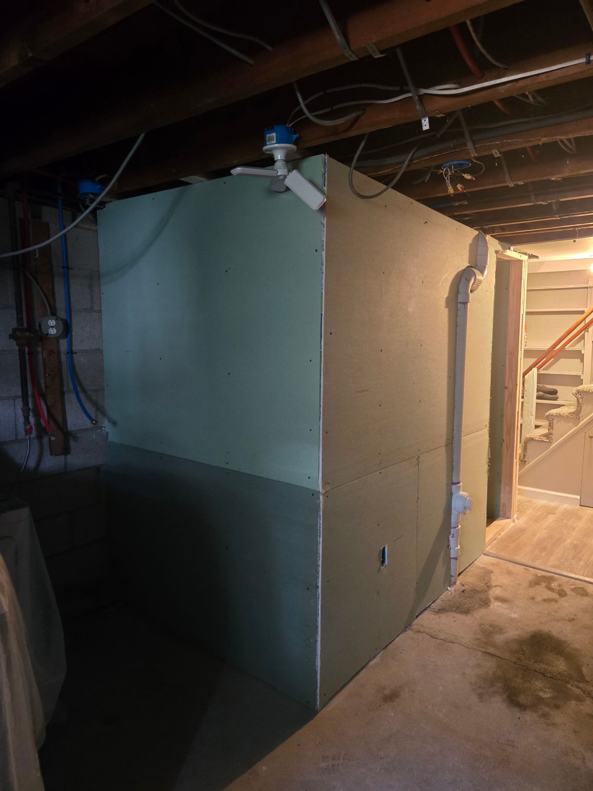 Large, green, boxy structure in a basement. It has pipes and wires, possibly containing a water tank or storage.