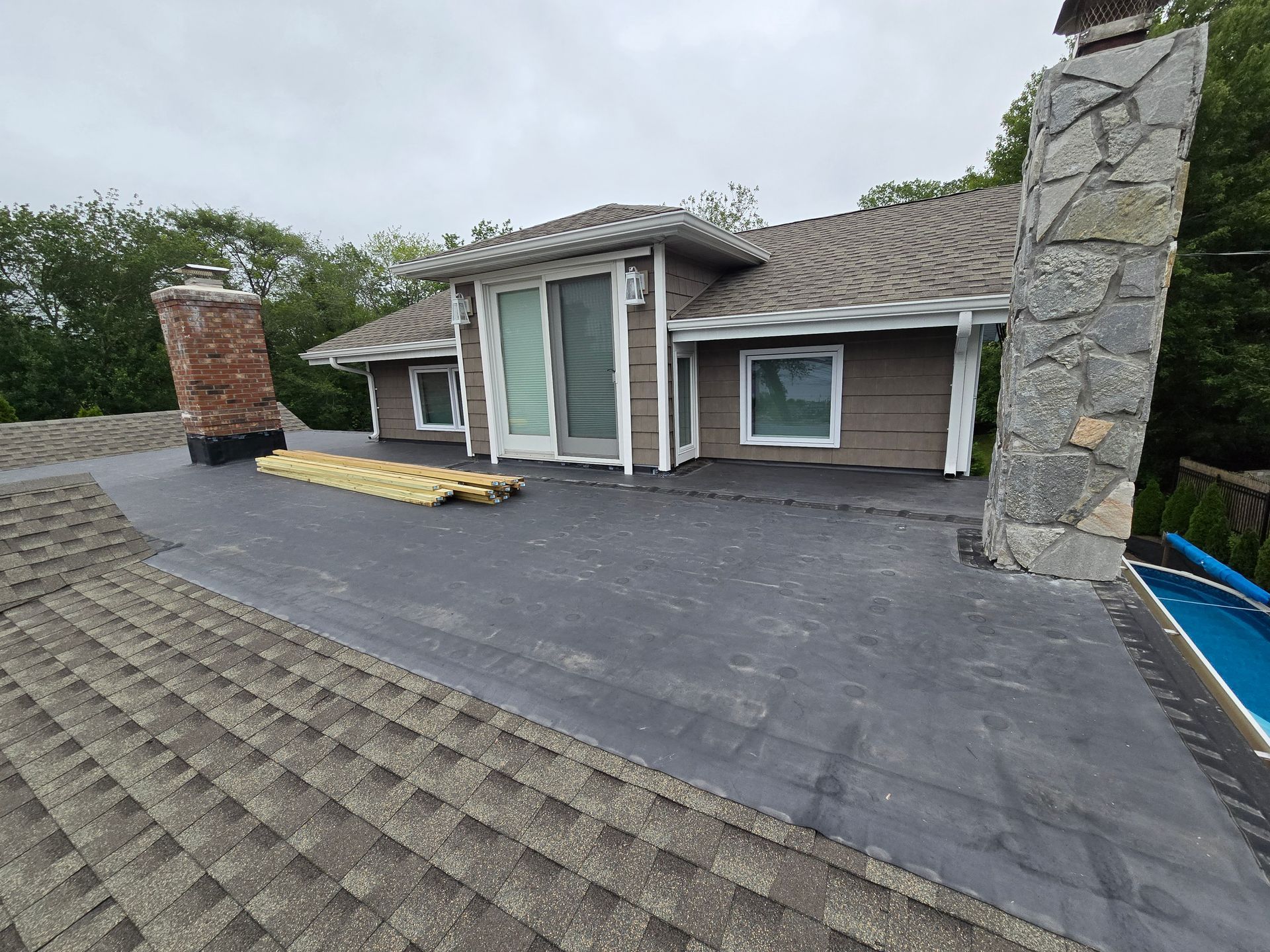 A house with a gray shingle roof, flat roof, and two chimneys. The sky is overcast.