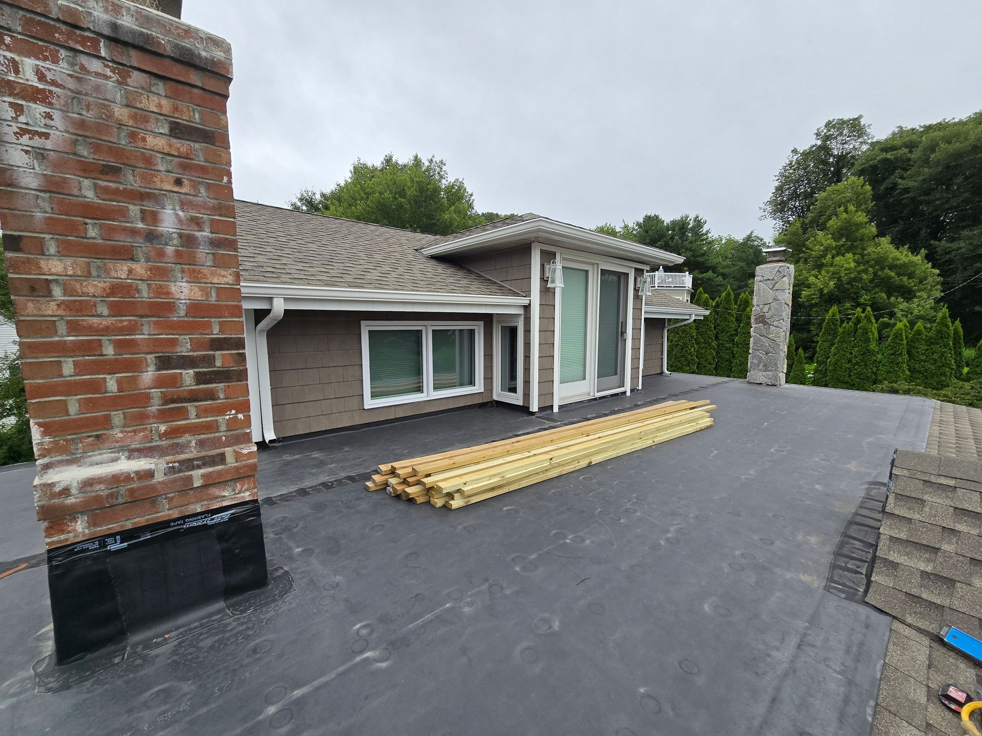 Rooftop with chimney, wooden planks, and building, against a cloudy sky.