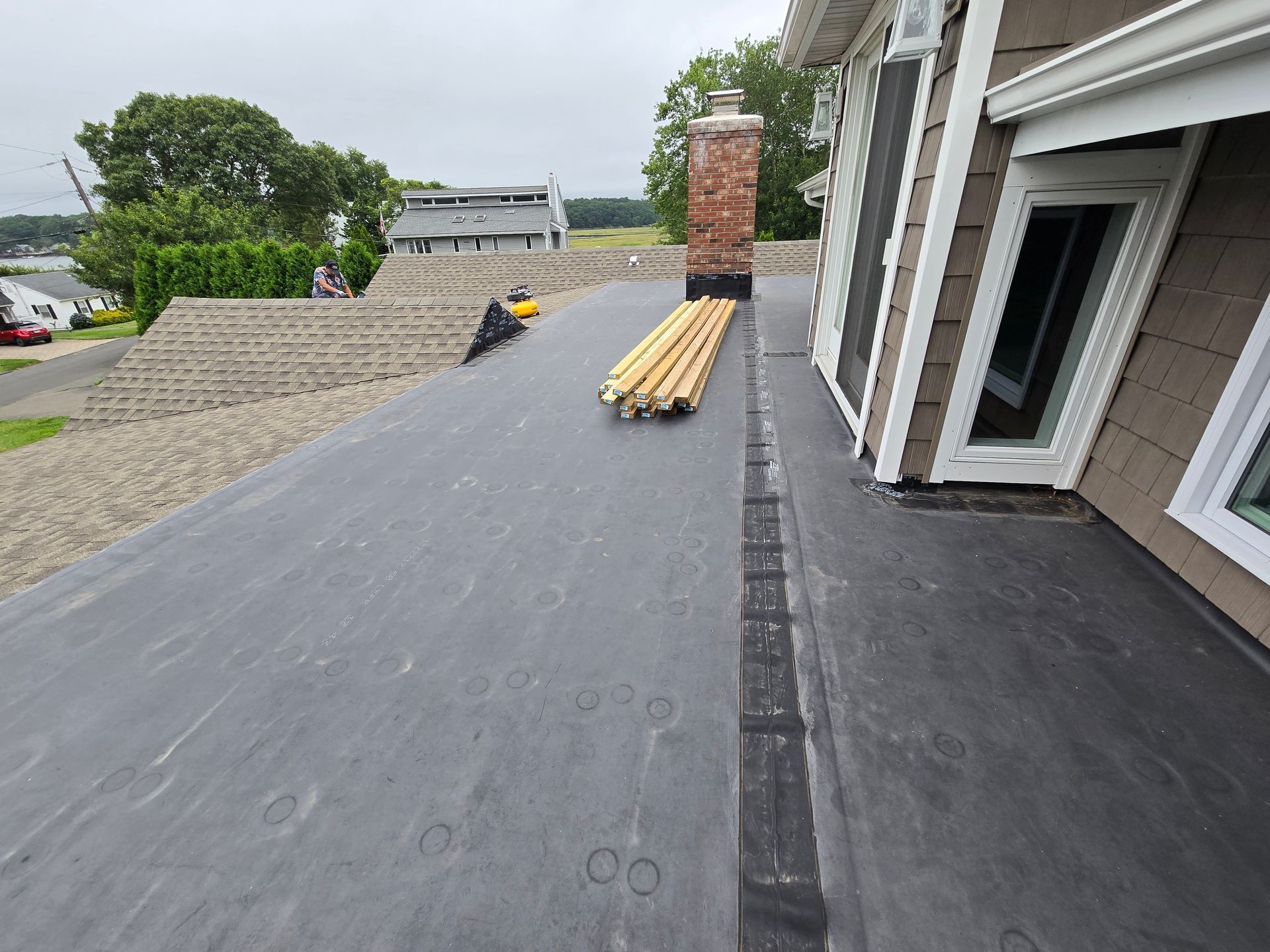 Flat roof with black surface; chimney, wooden beams, and house visible.