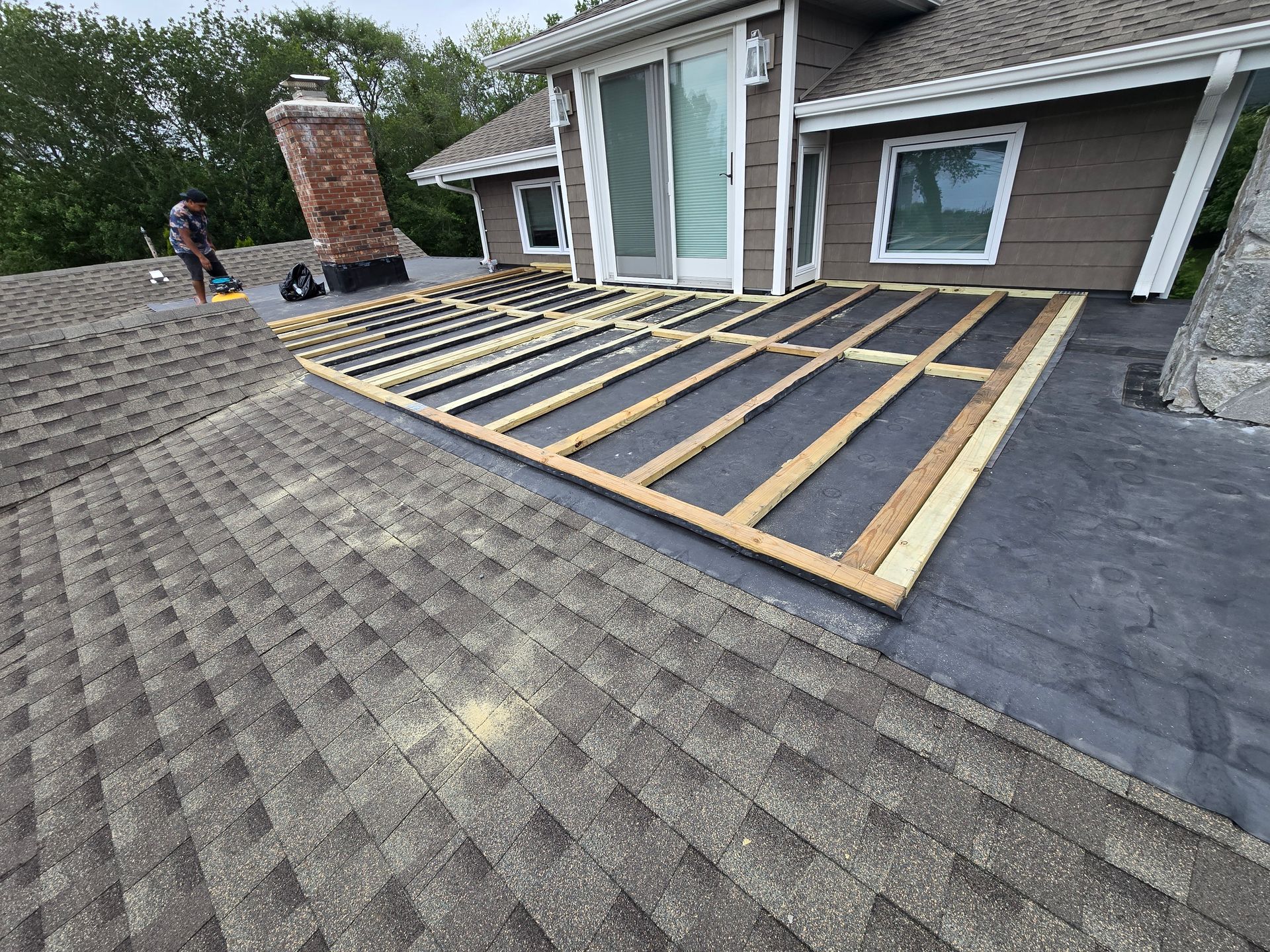 Construction of a rooftop deck on a house with brown shingles and a sliding glass door.