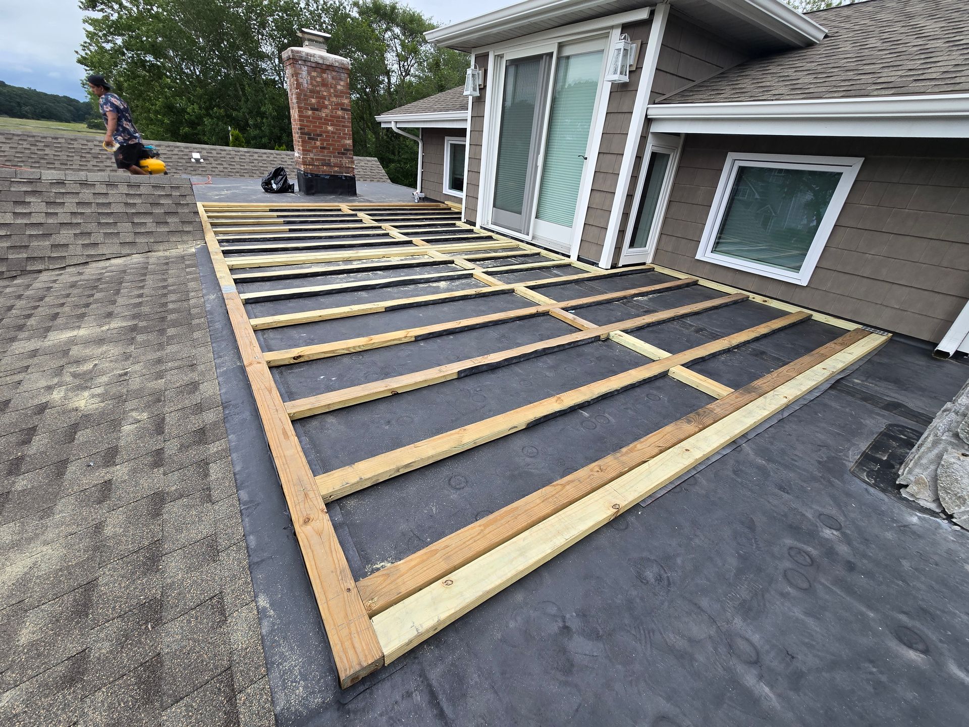 A rooftop deck frame being built next to a building. Gray roof, brown wood.
