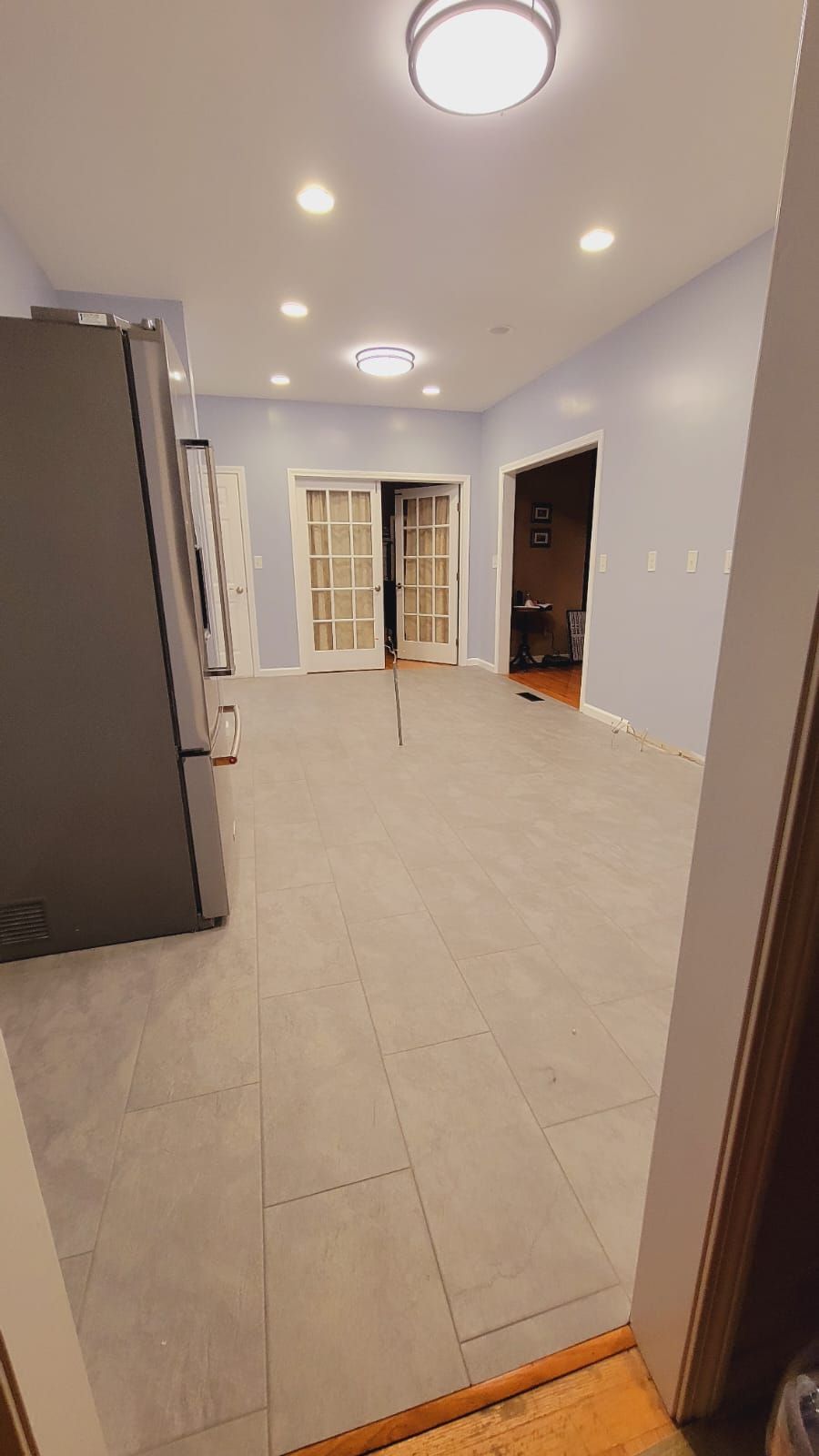Empty kitchen with gray tile floor, fridge, and French doors to a room.
