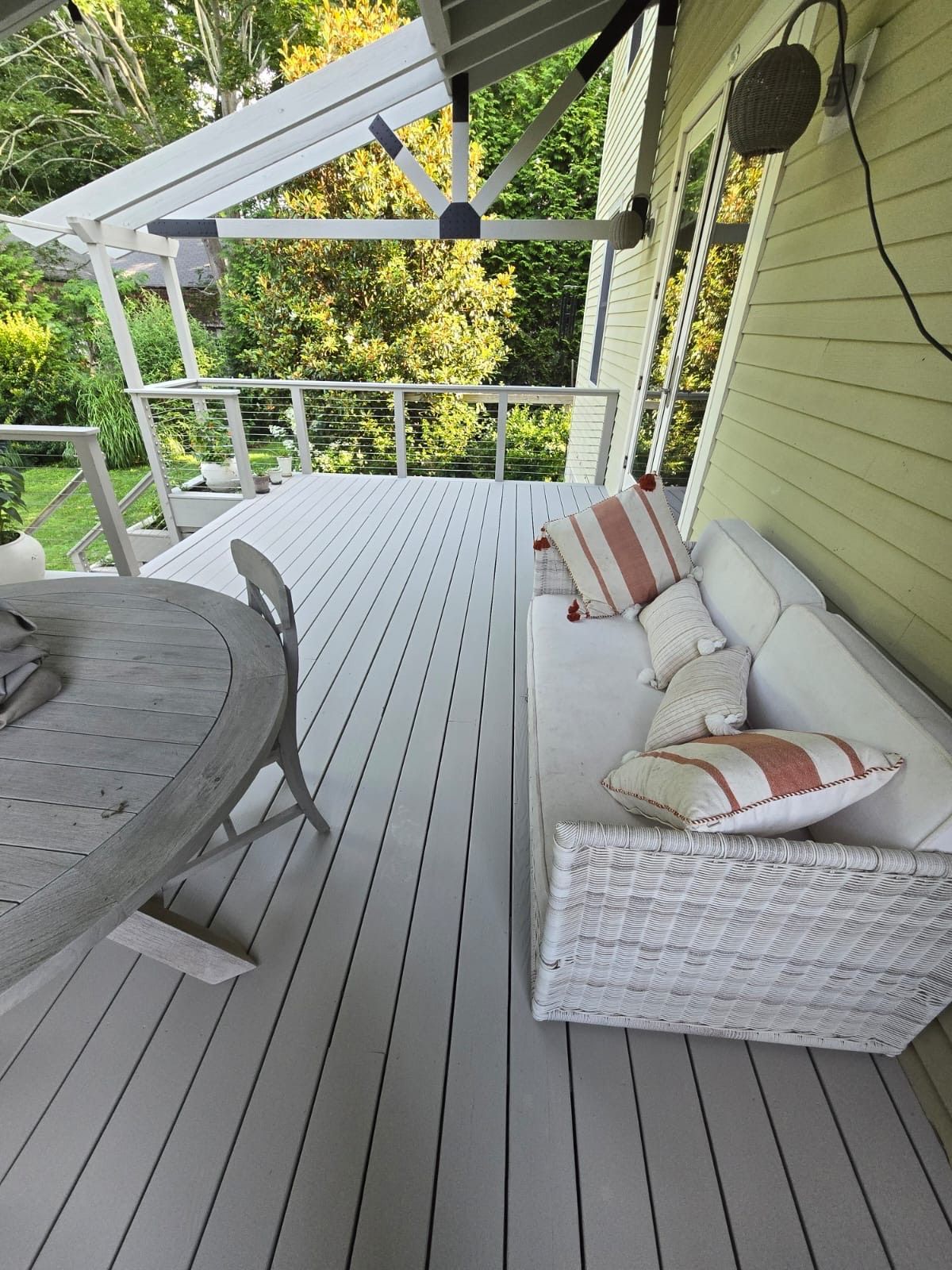 White outdoor deck with a seating area, a table, and a pergola roof, surrounded by trees.