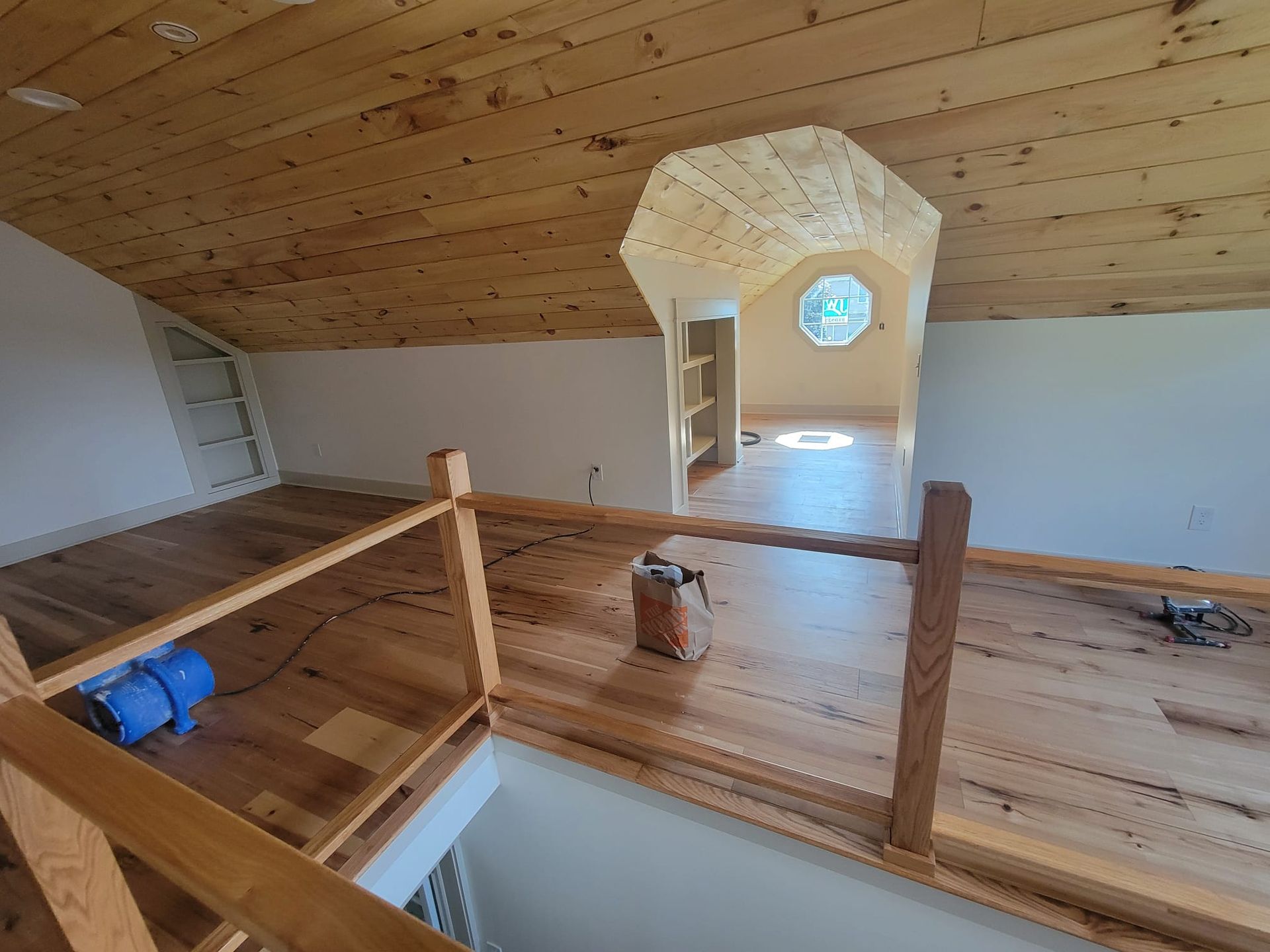 Loft with wood floors, railings, and a light-filled nook with a round window.