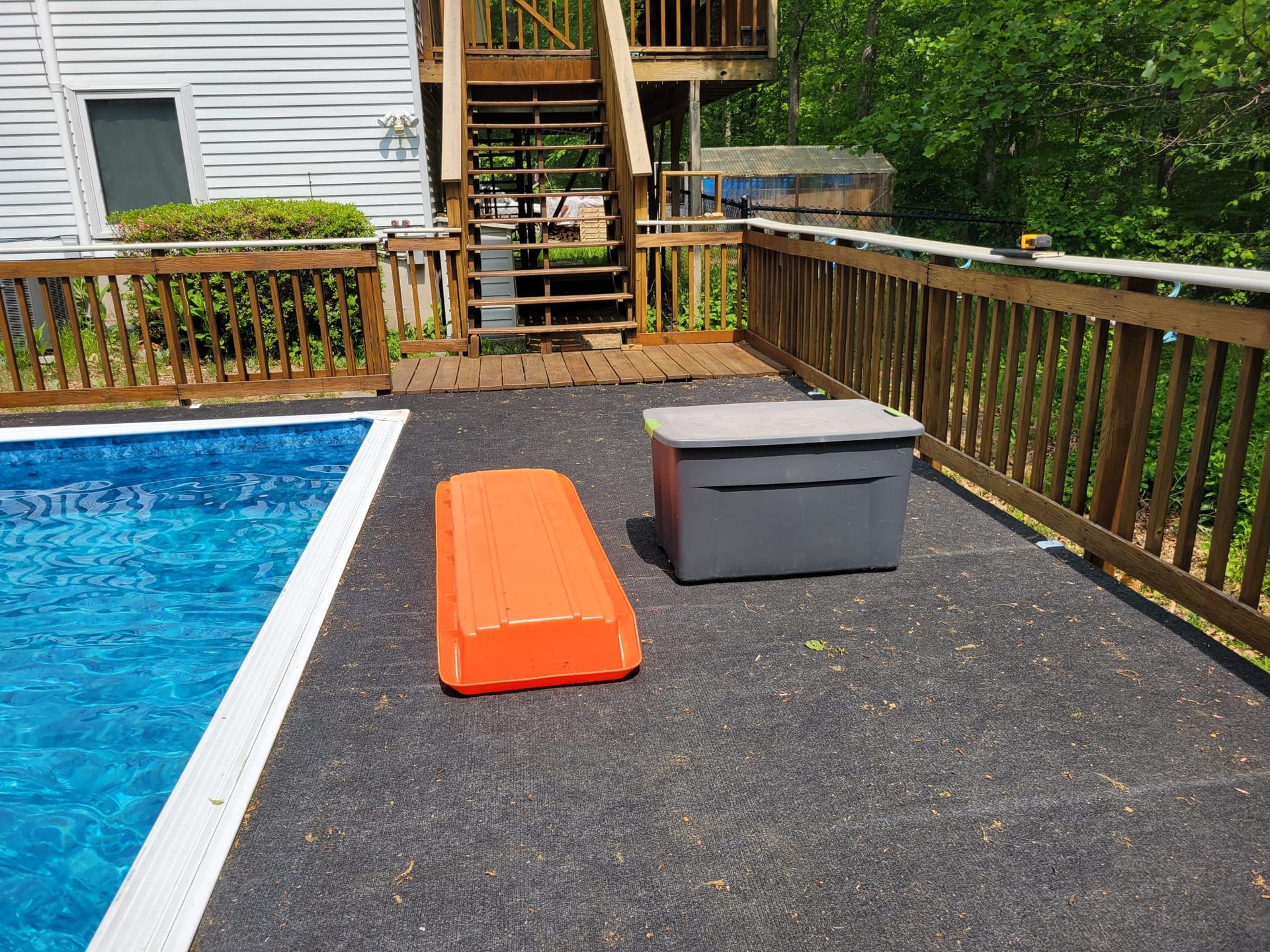 Poolside deck with orange float and grey storage box; pool on the left; stairs to the house in the background.