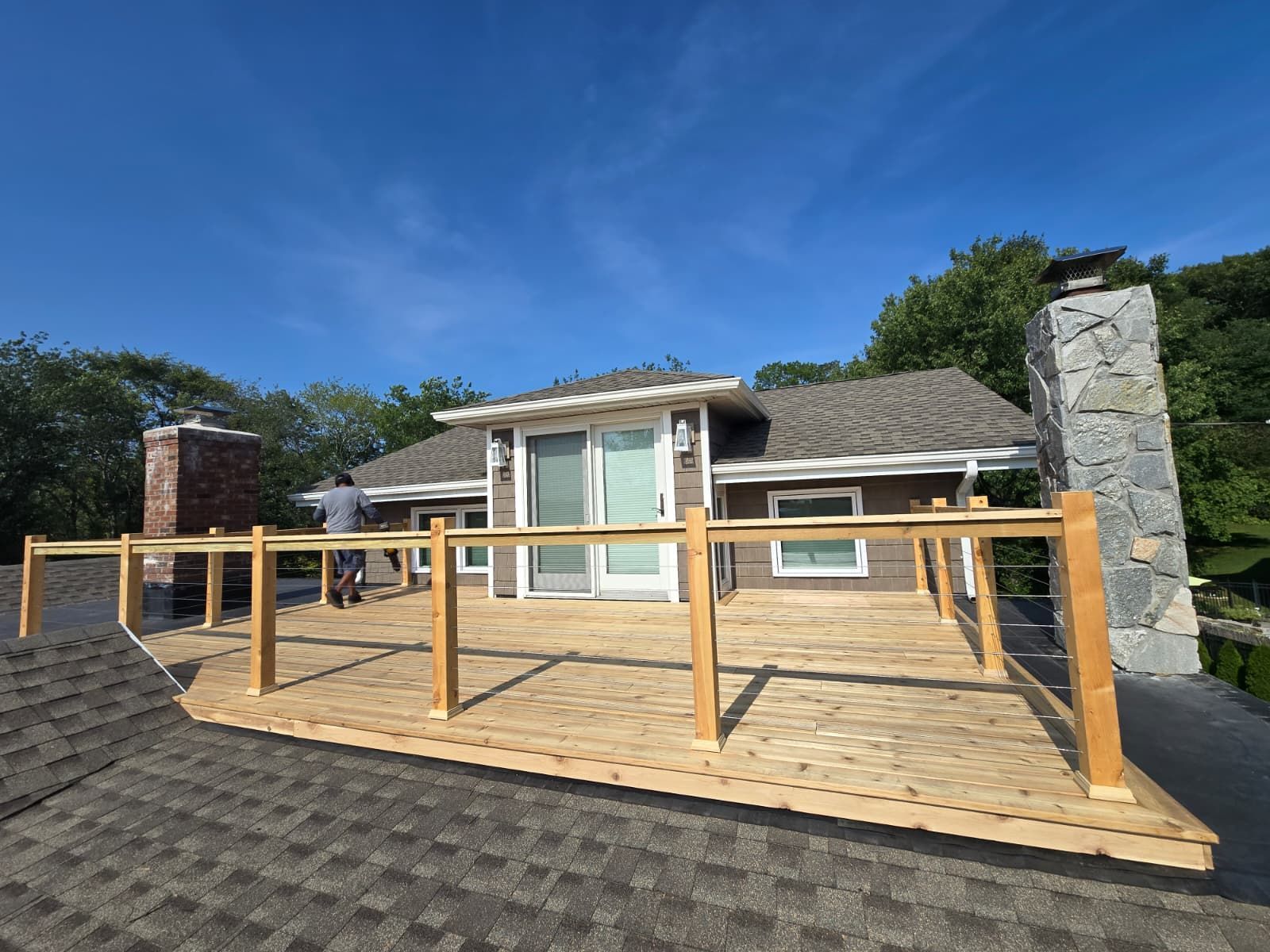 Rooftop deck with railing being built, overlooking a house with chimneys, under blue sky.