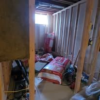 An unfinished basement with insulation rolls and wooden framing. A bright window is visible.