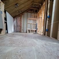 Interior view of a room under construction with unfinished wood flooring and walls.