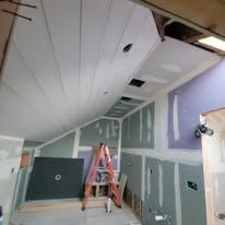 Construction site: attic with ladder, unfinished drywall, ceiling panels.