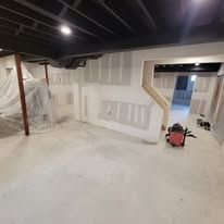 Basement under construction; drywall, black ceiling, red tool, unfinished.