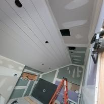 Interior view of a ceiling under construction, with wooden beams, drywall, and a ladder.