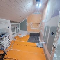 Interior view of a room under construction with orange flooring, exposed framing, and drywall.
