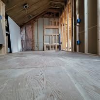 Empty attic space with unfinished wood flooring. Walls show studs and unfinished walls.