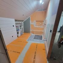 Bathroom renovation in progress: orange flooring, exposed walls, and a partially constructed shower area.