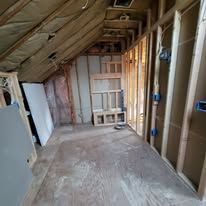 Interior of a room under construction, exposed wood frame, insulation, and unfinished walls.
