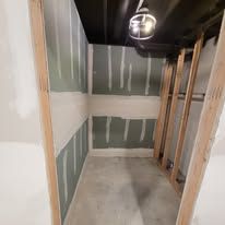 Unfinished interior room, drywall partially installed on walls. Cement floor, light fixture on ceiling.