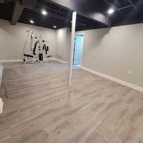A basement with light grey wood-look flooring, a workout machine, and a vertical white support beam.