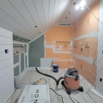 Renovation in progress, dusty room with vacuum, exposed walls, and wooden ceiling.